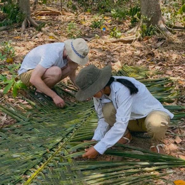 Jenny and Jonas weaving palm leaves to build a cow shed.